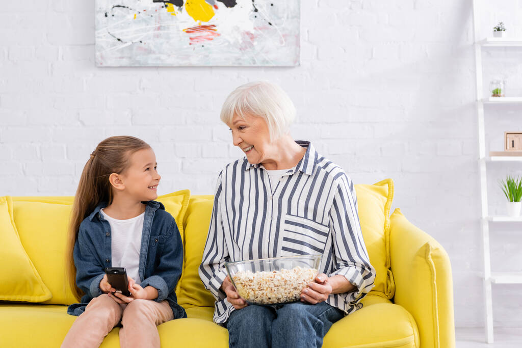 Enfant souriant avec télécommande regardant mamie avec pop-corn  - Photo, image