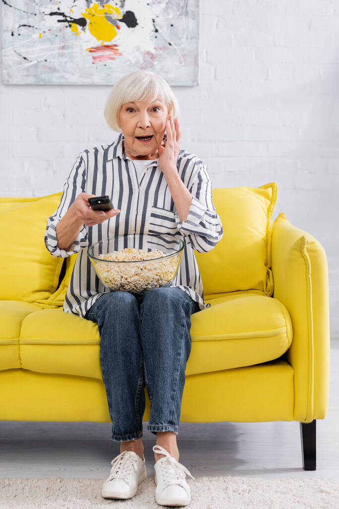 Волнующая женщина с попкорном и пультом дистанционного управления смотрит телевизор  - Фото, изображение