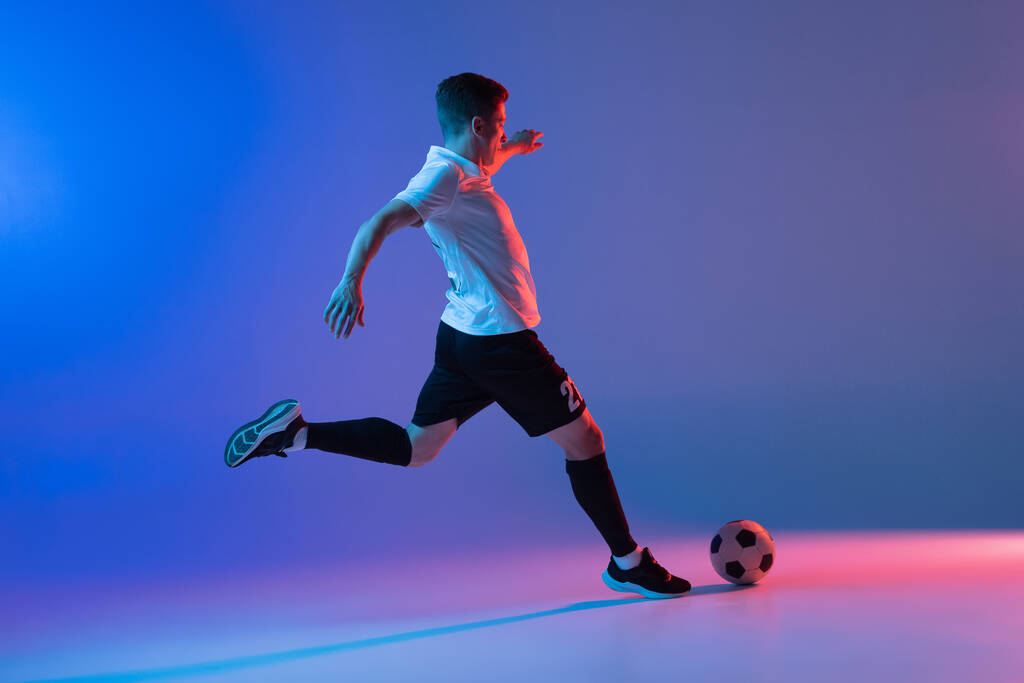 ネオンライトのグラデーションブルーピンクの背景に隔離されたアクションと動きで1人の男性サッカー選手 - 写真・画像