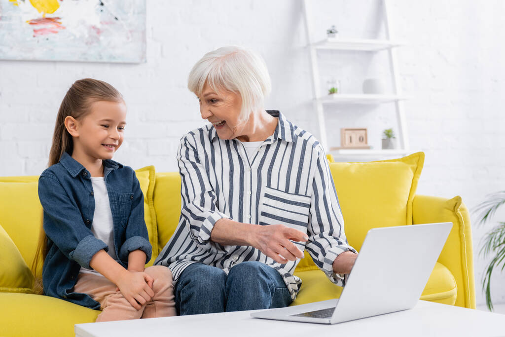 Положительная бабушка указывает на ноутбук рядом с девушкой  - Фото, изображение