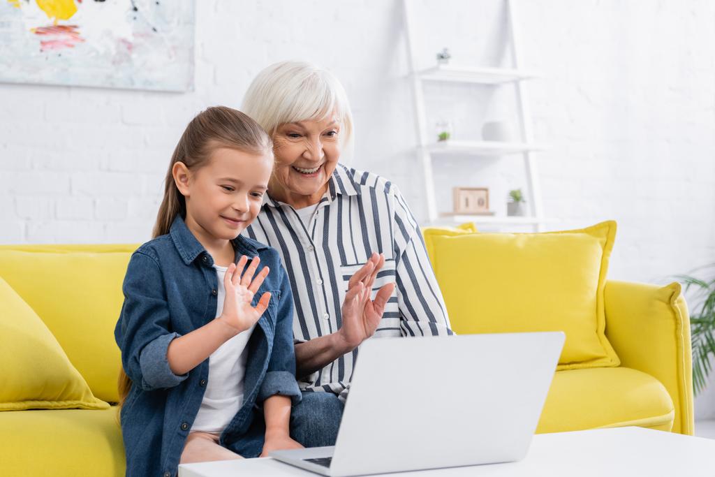 Hymyilevä isoäiti ja lapsi, jolla on videopuhelu kannettavalla tietokoneella kotona  - Valokuva, kuva