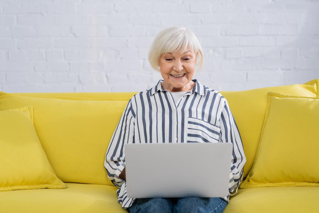 Ältere Telearbeiter lächeln und schauen auf Laptop, während sie von zu Hause arbeiten - Foto, Bild