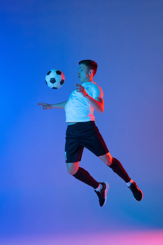 Un jugador de fútbol masculino en acción y movimiento aislado sobre fondo azul degradado rosa en luz de neón - Foto, imagen