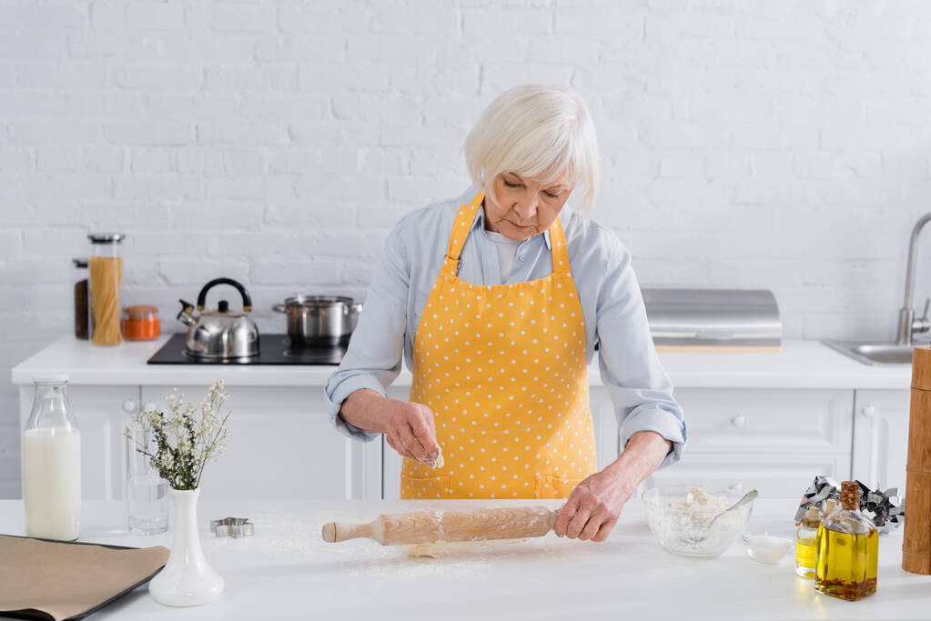 Seniorin gießt in Küche Mehl auf Nudelholz - Foto, Bild