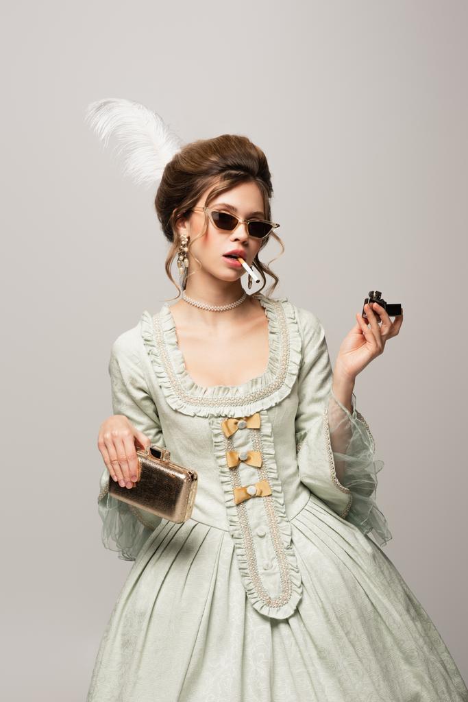 młoda kobieta w vintage strój i modne okulary przeciwsłoneczne palenie papierosów odizolowany na czarny - Zdjęcie, obraz