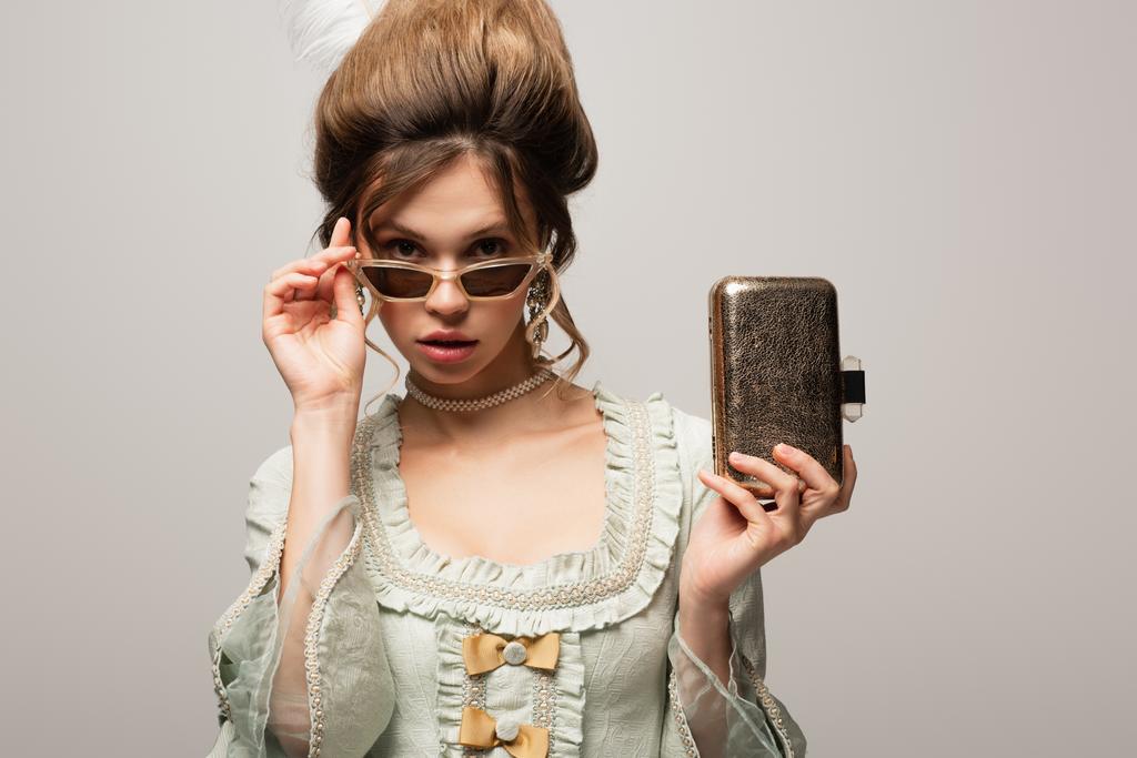 Hübsche Frau im Retro-Kleid und moderner Sonnenbrille mit goldener Handtasche - Foto, Bild