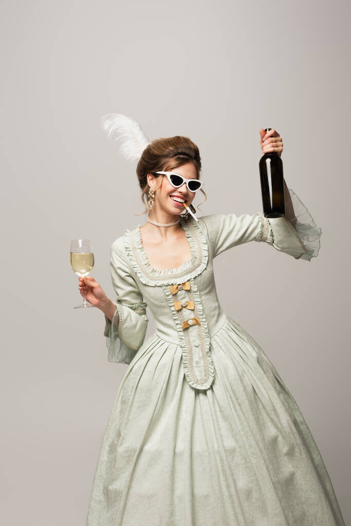 vidám nő vintage ruhában pózol bor és cigaretta elszigetelt szürke - Fotó, kép