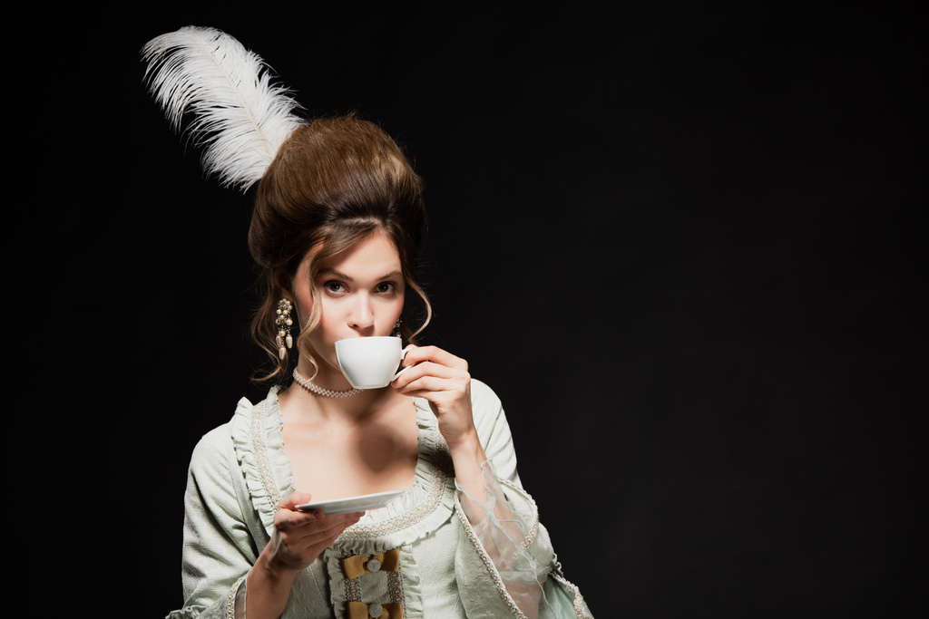 элегантная женщина в ретро-костюме пьет кофе, изолированный от черного - Фото, изображение