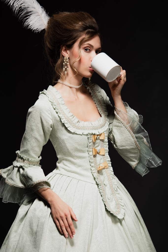 hübsche Frau im eleganten Vintage-Kleid trinkt Tee isoliert auf schwarz - Foto, Bild