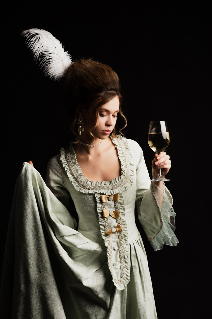 elegante mujer en vestido retro posando con copa de vino blanco aislado en negro - Foto, imagen