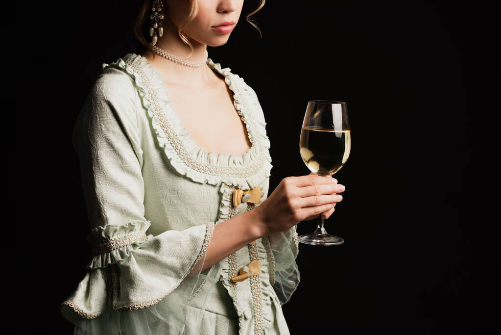 vista parcial de mujer joven en vestido retro sosteniendo vaso de vino blanco aislado en negro - Foto, imagen