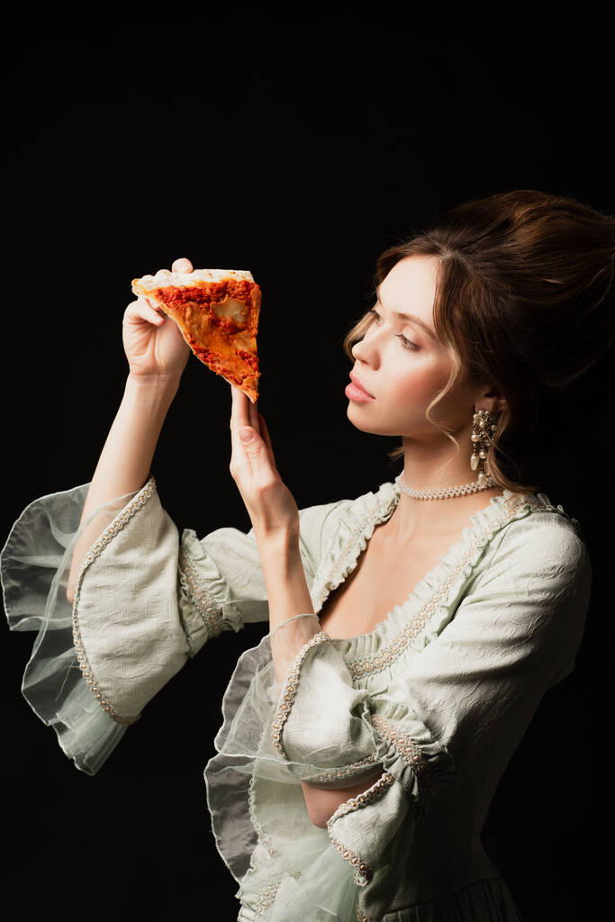 elegancka kobieta w vintage strój patrząc na pyszne pizzy izolowane na czarno - Zdjęcie, obraz
