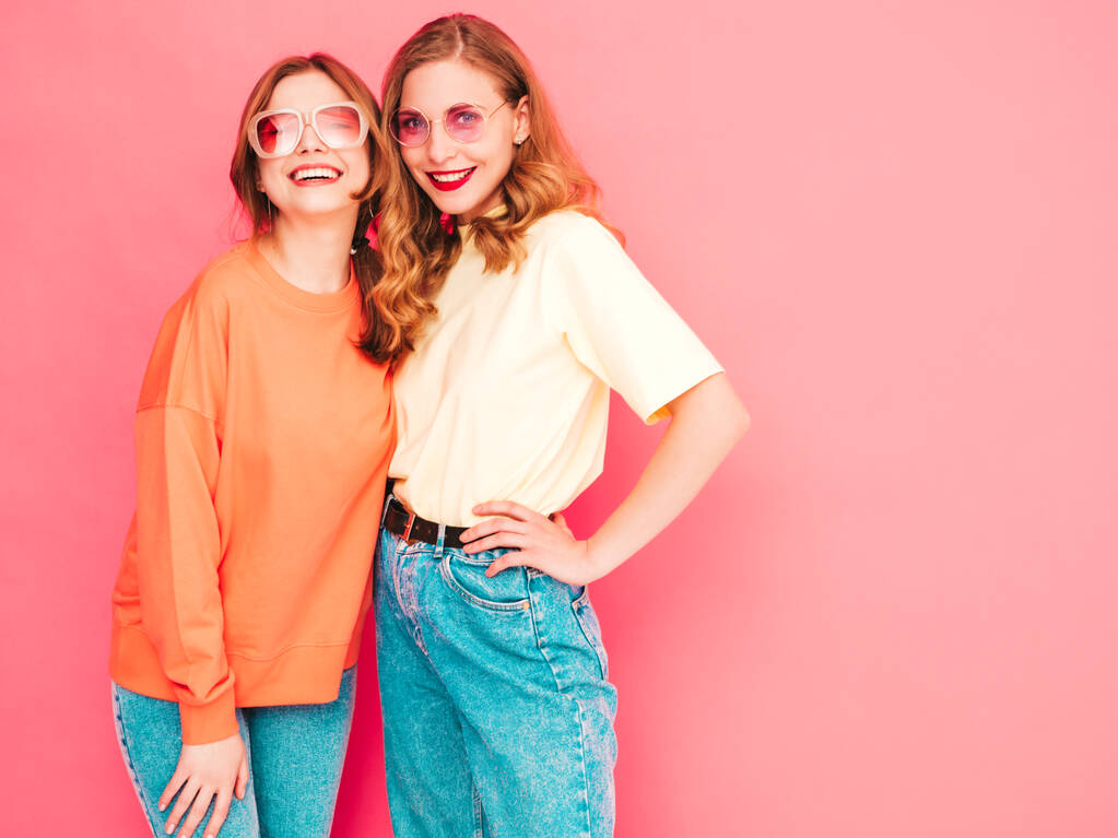 Deux jeunes belles hipsters souriantes en vêtements tendance d'été. Sexy femmes insouciantes posant près du mur rose en studio. Modèles à la mode et positifs s'amuser. Joyeux et heureux - Photo, image