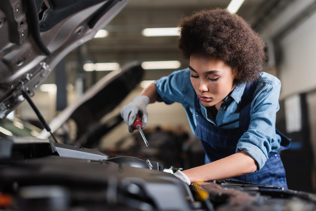 young african american mechanic repairing car motor with screwdriver in garage - Photo, Image