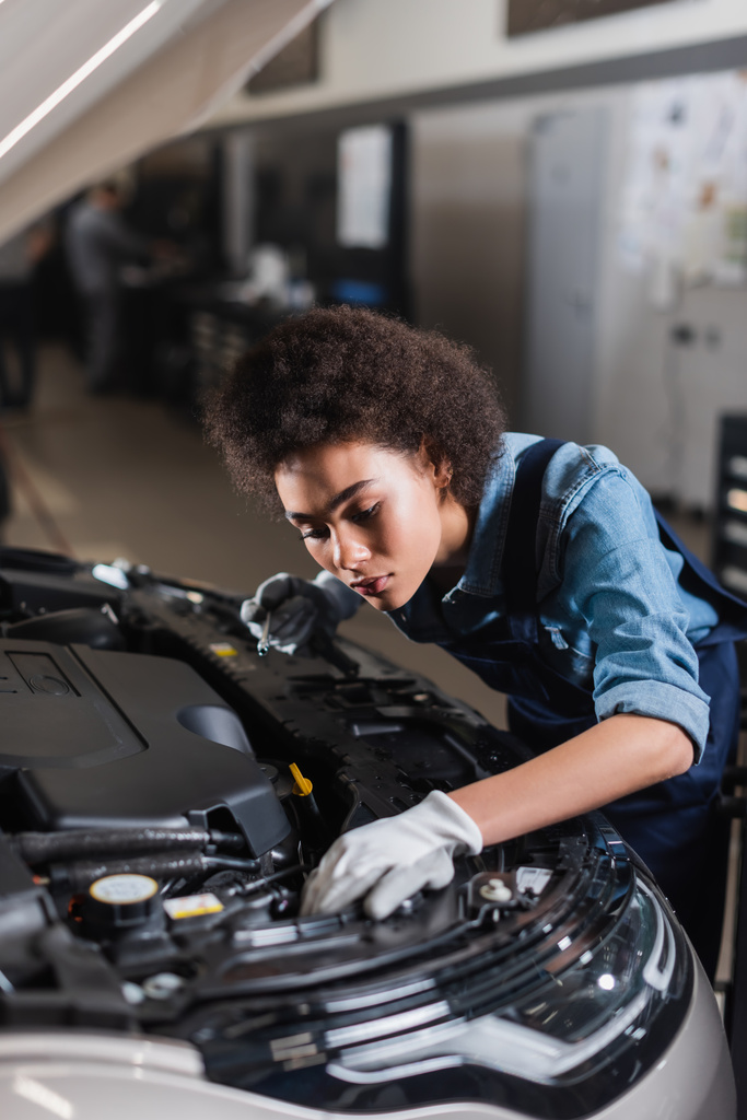 junger afrikanisch-amerikanischer Mechaniker hält Schraubenschlüssel und fixiert Automotor in Garage - Foto, Bild