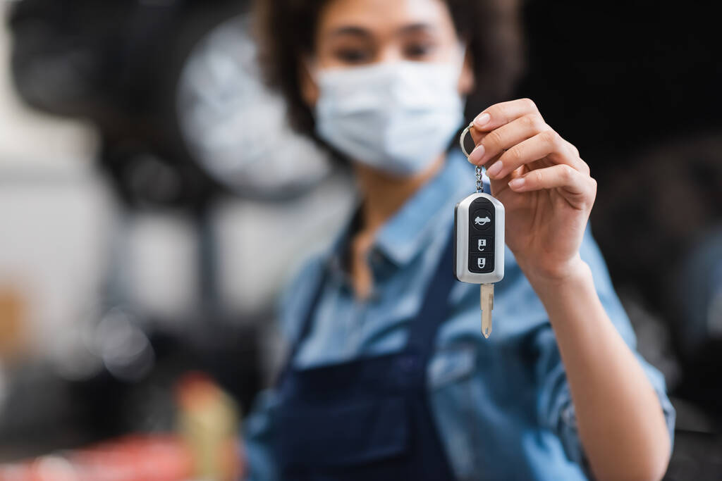 car key in hand of blurred young african american mechanic in protective mask in garage - Photo, Image
