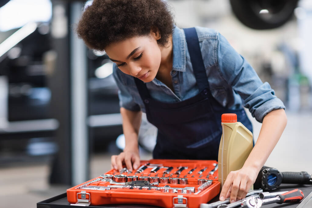 молодой африканский американский механик выбирает оборудование из ящика с инструментами в гараже - Фото, изображение