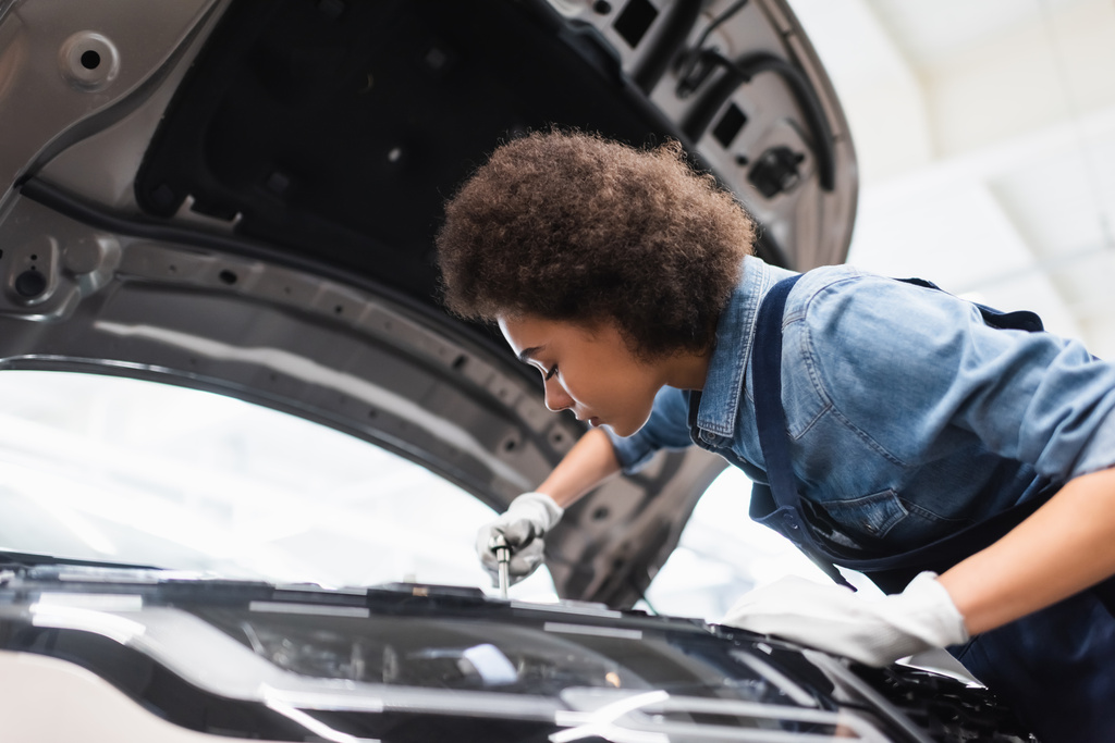 Genç Afro-Amerikan tamirci garajı açık kapüşonlu bir arabada motor tamir ediyor. - Fotoğraf, Görsel