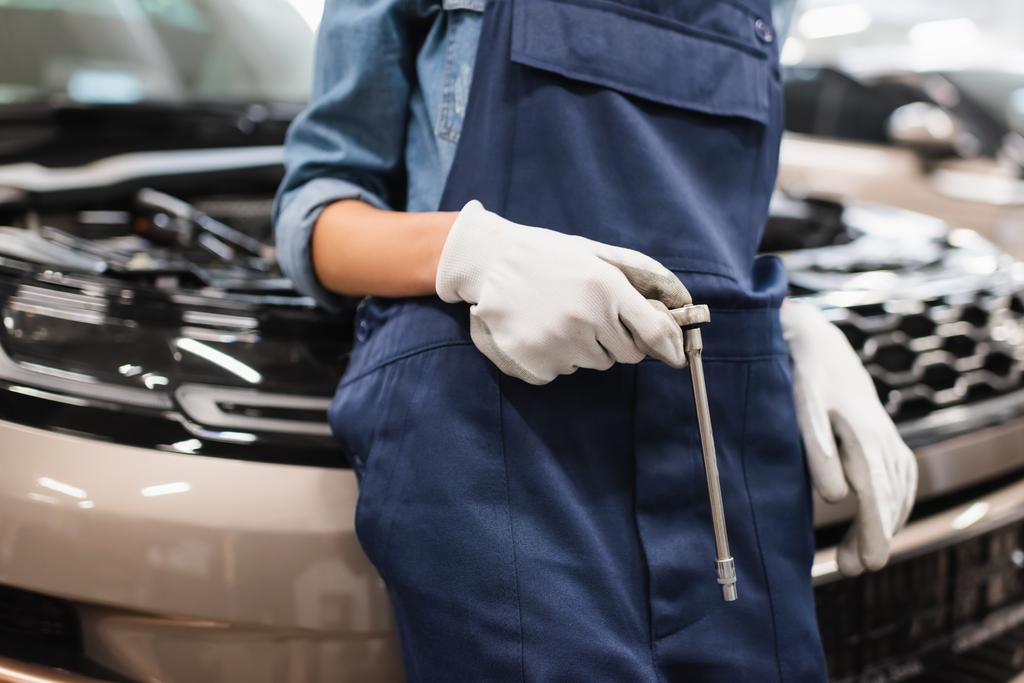 vista parcial de la joven mecánica afroamericana sosteniendo la llave y de pie cerca del coche en servicio de reparación de automóviles - Foto, imagen