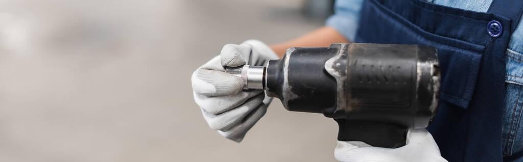 close up view of mechanic hands in gloves holding electric screwdriver and attachment on blurred background, banner - Photo, Image