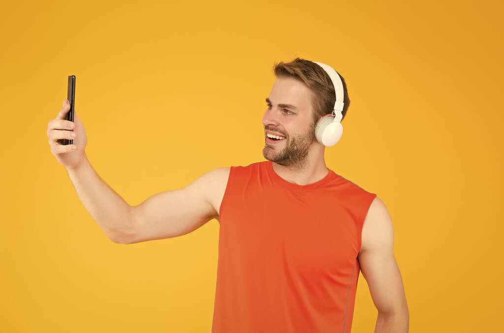 スポーツウェアの幸せな若い男は、現代のヘッドフォンリスニング音楽を着用しながら、トレーニングは、自撮りのためのスマートフォンを使用します,デジタルスポーツ - 写真・画像