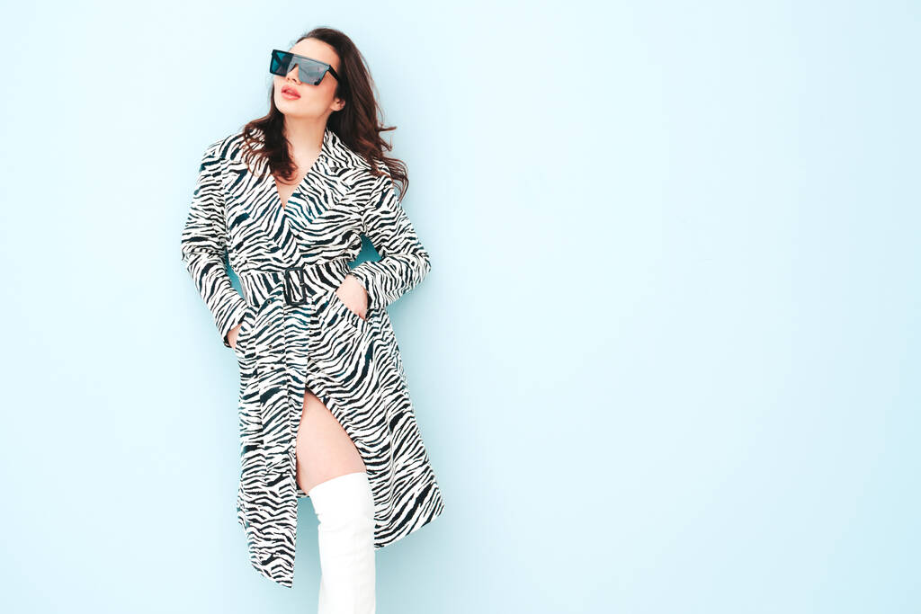 High fashion portret van jonge mooie brunette vrouw dragen mooie trendy zomer zebra coat.Sexy mode model poseren in de buurt van lichtblauwe muur in studio.Modieuze vrouw binnen in een zonnebril - Foto, afbeelding