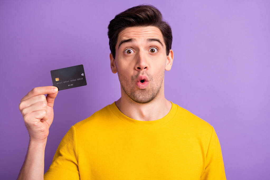 Foto do jovem bonito cara surpreendido chocado segurar pagamento de cartão de crédito isolado sobre fundo cor violeta - Foto, Imagem