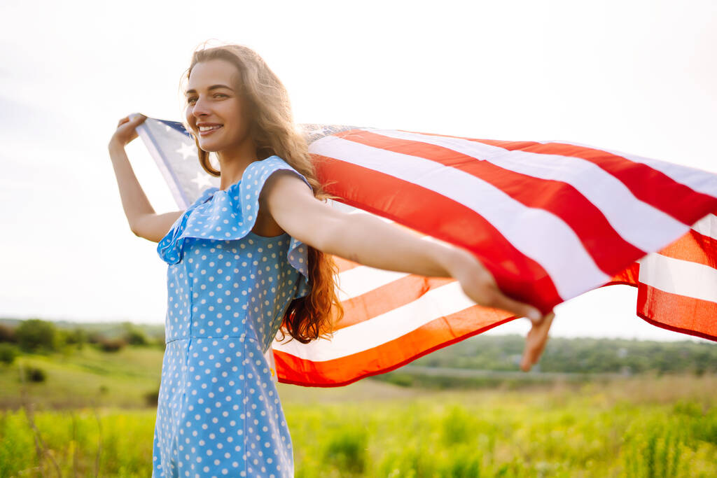Giovane donna con bandiera americana sul prato fiorito. Il 4 luglio. Il giorno dell'indipendenza. Vacanza patriottica. Bandiera USA sventola nel vento. - Foto, immagini