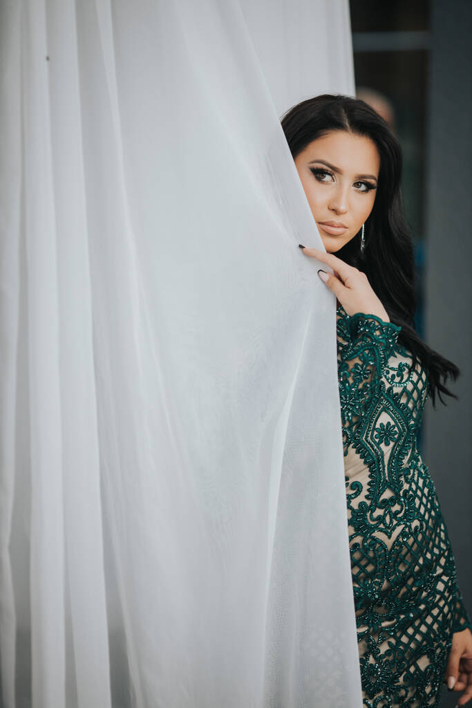 Uma jovem mulher atraente em um vestido curto segurando a cortina e posando - Foto, Imagem