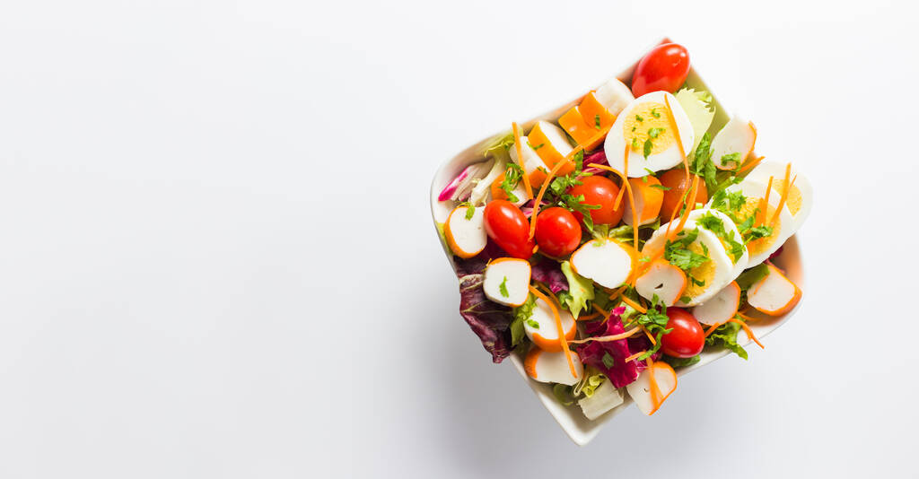 Ein Blick von oben auf den köstlichen und frisch zubereiteten Salat L 'Oceane in einer Schüssel auf der weißen Oberfläche - Foto, Bild