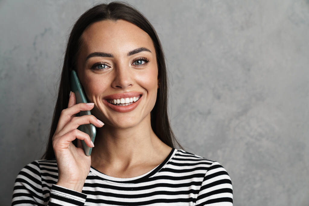 Портрет улыбающейся повседневной женщины, держащей смартфон на синем фоне, звонящей - Фото, изображение
