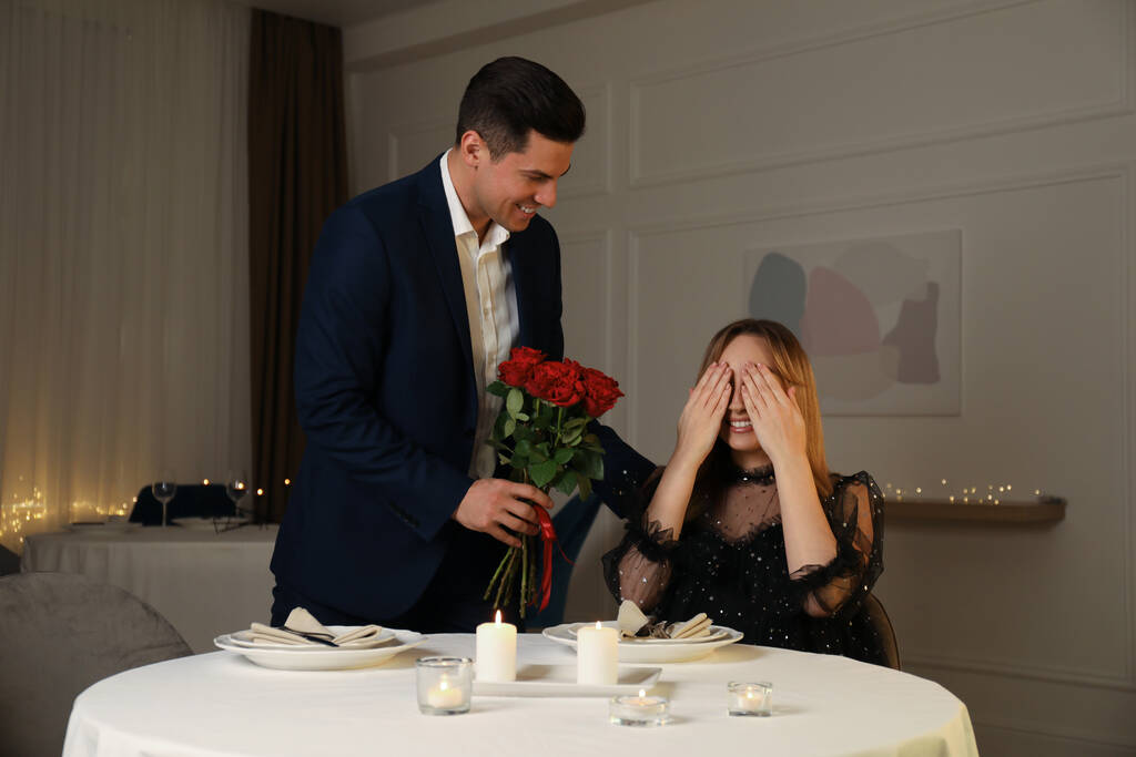 Man presenting roses to his beloved woman in restaurant at romantic dinner - Photo, Image