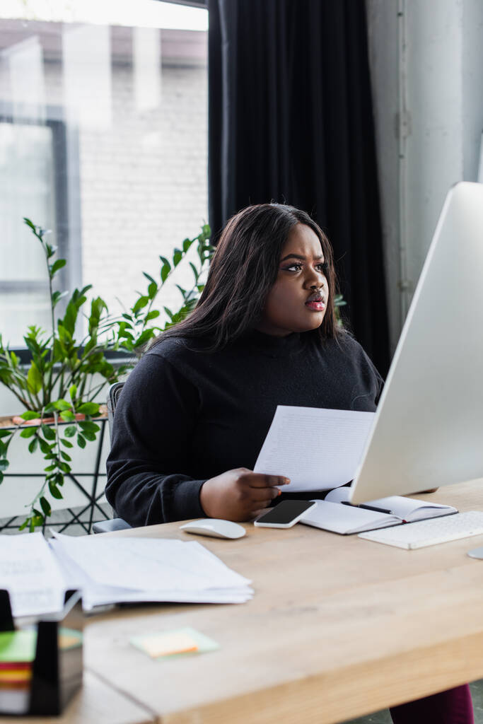 集中アフリカ系アメリカ人とオフィスのコンピュータモニターを見ているサイズのビジネス女性  - 写真・画像