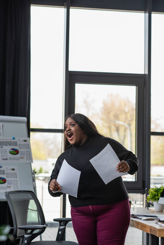 sorprendido afroamericano más tamaño mujer de negocios con documentos en la oficina - Foto, Imagen