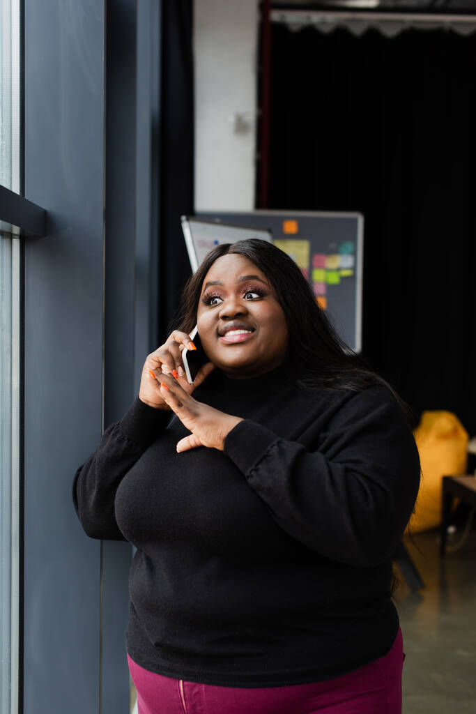 alegre afroamericana más tamaño mujer de negocios hablando en teléfono inteligente en la oficina - Foto, imagen