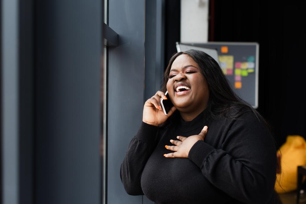 χαμογελαστή Αφροαμερικανίδα συν μέγεθος γυναίκα μιλάει στο κινητό στο γραφείο - Φωτογραφία, εικόνα