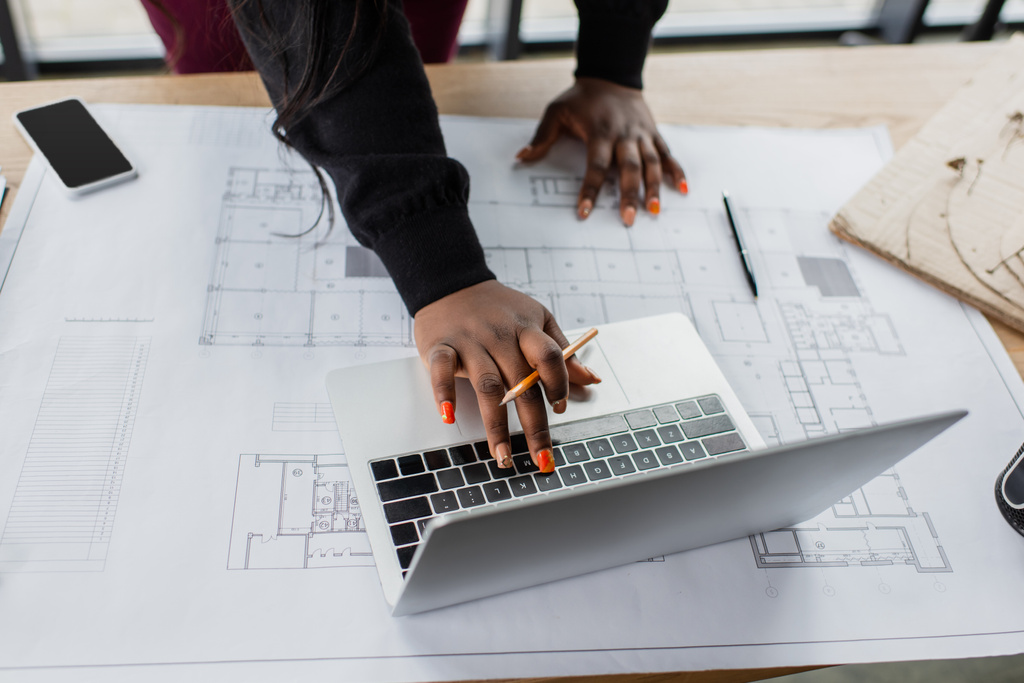 Ausgeschnittene Ansicht einer afrikanisch-amerikanischen Ingenieurin mit Laptop in der Nähe des Bauplatzes auf dem Schreibtisch - Foto, Bild