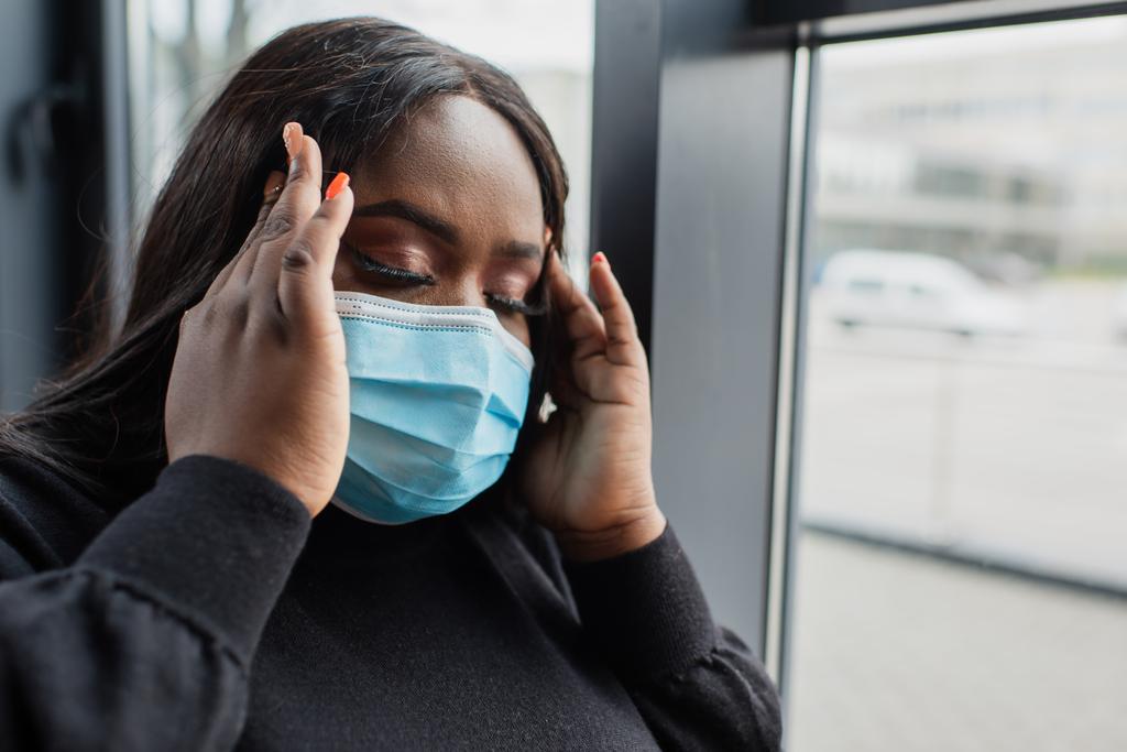 Africano americano más tamaño mujer de negocios en máscara médica con dolor de cabeza en la oficina - Foto, Imagen