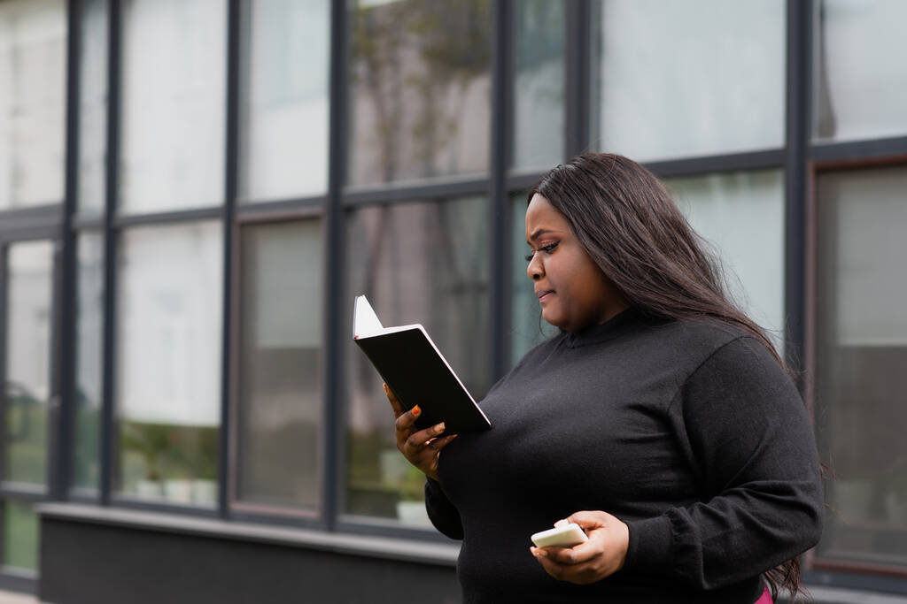 africano americano más tamaño mujer sosteniendo portátil y teléfono inteligente fuera  - Foto, Imagen