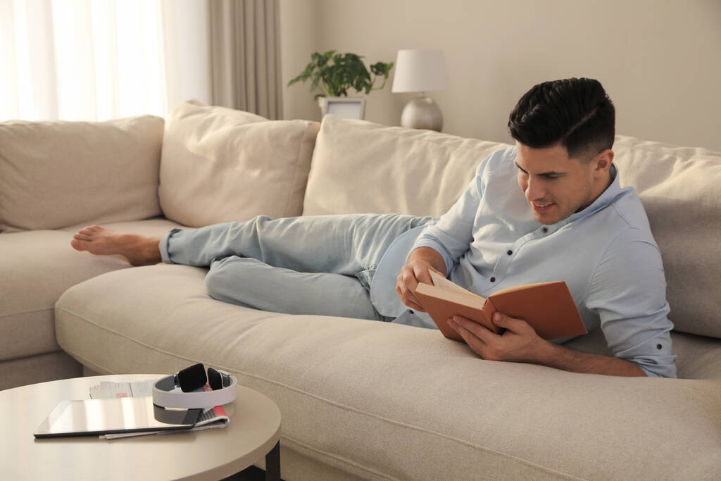 Ο άνθρωπος διαβάζει βιβλίο στον καναπέ στο σαλόνι - Φωτογραφία, εικόνα