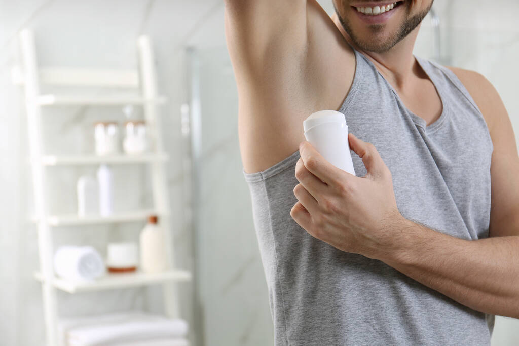 Mężczyzna stosujący dezodorant w łazience, zbliżenie. Miejsce na tekst - Zdjęcie, obraz