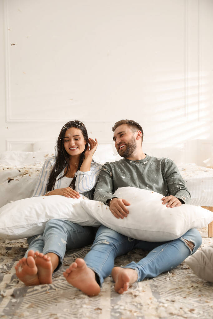 Szczęśliwa młoda para odpoczywa po zabawnej walce na poduszki w sypialni - Zdjęcie, obraz