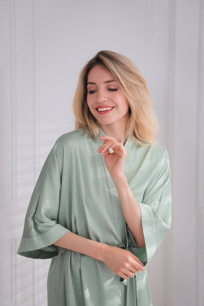 Mujer joven bonita en hermosa túnica de seda verde claro cerca de la pared blanca en el interior - Foto, imagen