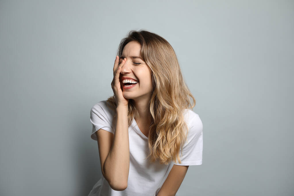 Veselá mladá žena se směje na šedém pozadí - Fotografie, Obrázek