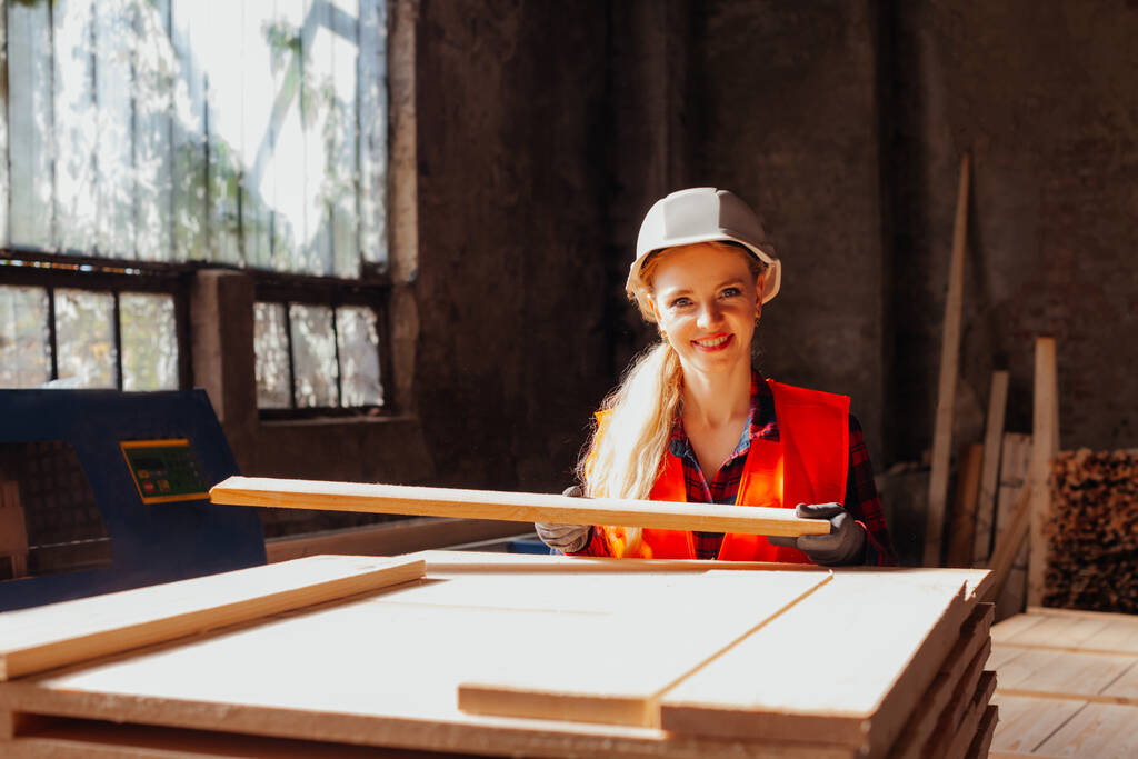 Atrakcyjna kobieta stolarka pracownik fabryki trzymający drewniane deski - Zdjęcie, obraz