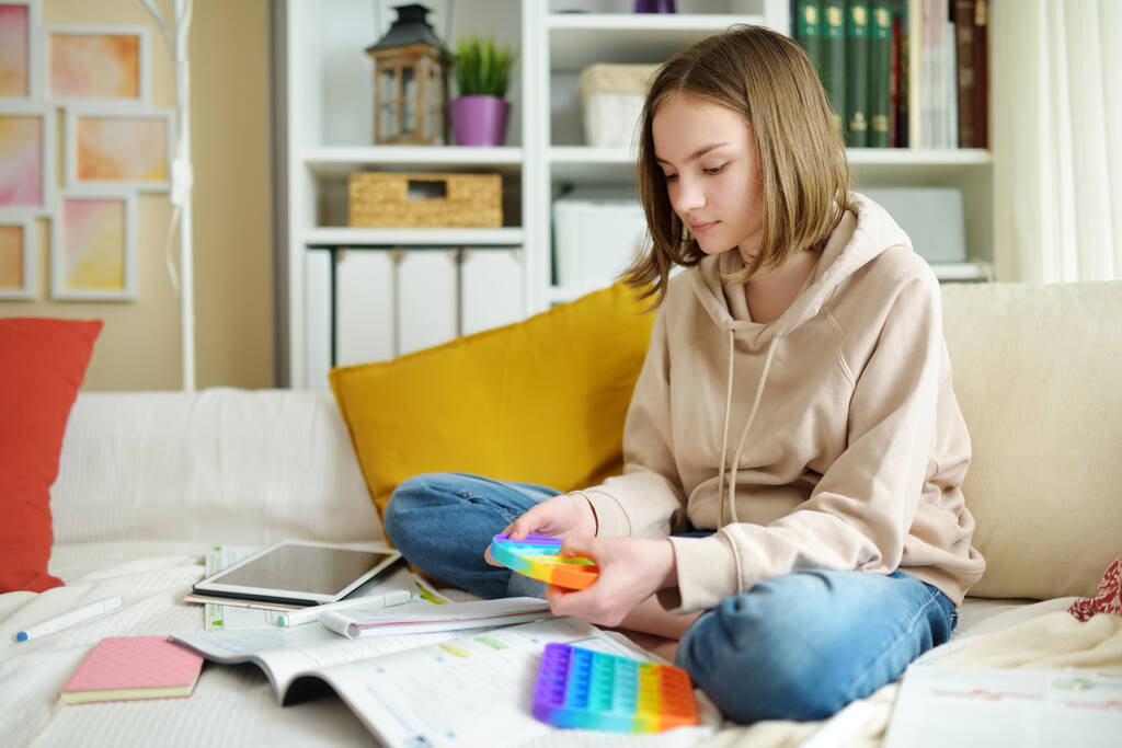 Teenagermädchen spielt zu Hause mit Regenbogen-Fidget-Spielzeug. Teen-Kind mit trendigen Stress und Angstlinderung zappeliges Spiel. Knallen die Grübchen des sensorischen Silikonspielzeugs. - Foto, Bild