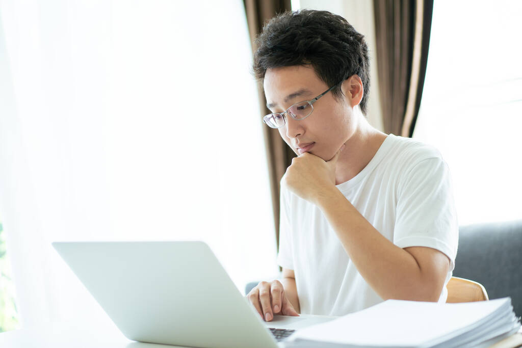 Felismerhetetlen ázsiai fiatalember, aki a laptop billentyűzetén dolgozik és gépel. Egy férfi, aki jegyzetfüzetet használ az irodában. Üzletember otthon dolgozik. - Fotó, kép