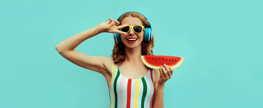 Summer portrait of cheerful happy smiling young woman in headphones listening to music with juicy slice of watermelon on a blue background - Photo, image
