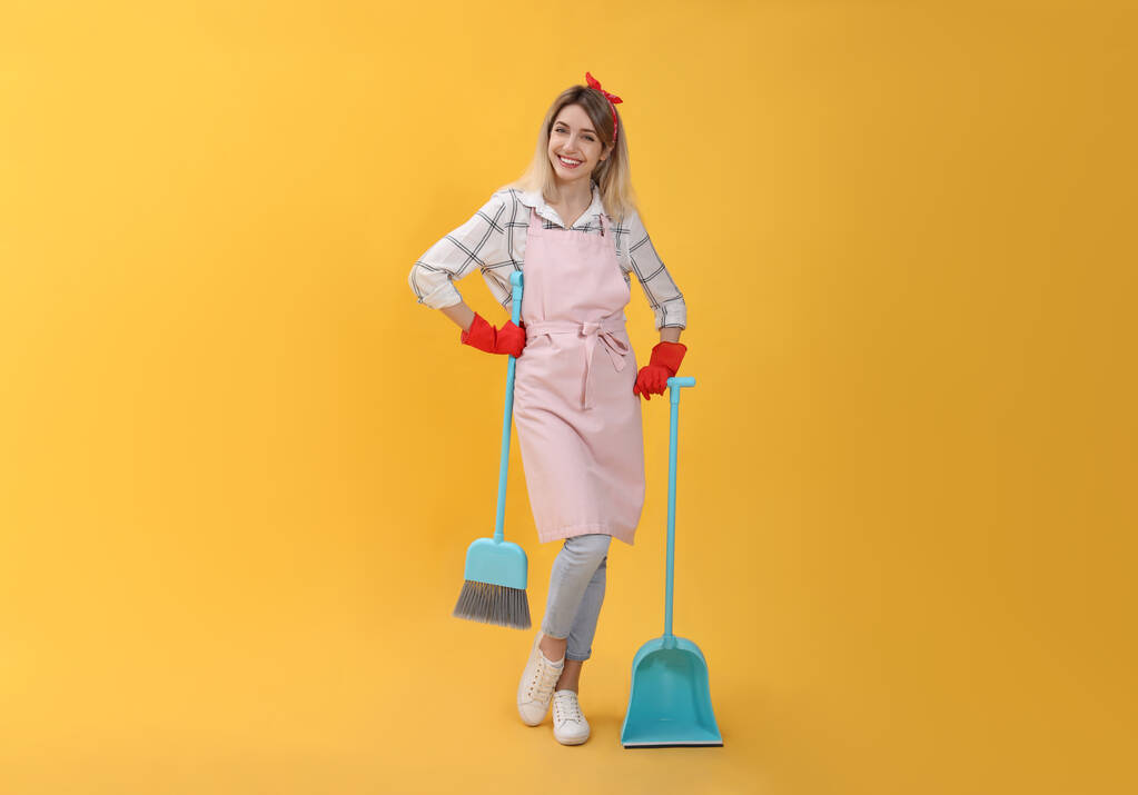 Junge Hausfrau mit Besen und Kehrschaufel auf gelbem Hintergrund - Foto, Bild