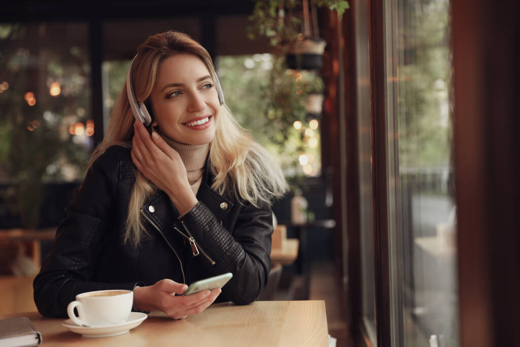 Jeune femme avec écouteurs et smartphone à l'écoute de la musique dans le café - Photo, image